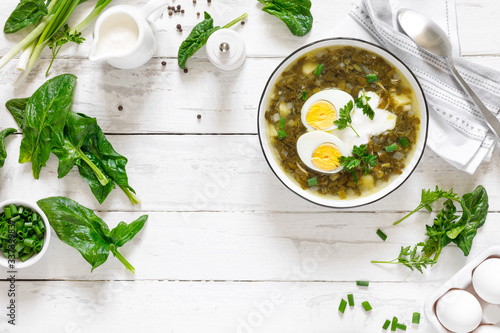 Green sorrel and spinach soup with boiled egg and sour cream on white wooden rustic table, top view