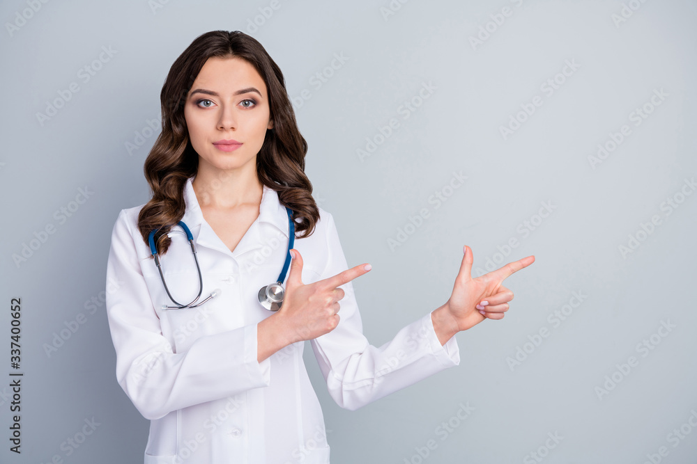 Photo of attractive family doc experienced lady virology clinic direct fingers empty space show pandemic rules disinfection wear lab coat stethoscope isolated grey color background Photo of attractive family doc experienced lady virology clinic direct fingers empty space show pandemic rules disinfection wear lab coat stethoscope isolated grey color background