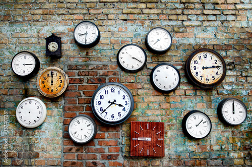 A lot of vintage clocks of different sizes hanging on a grunge brick wall. Round and square clocks show different time.