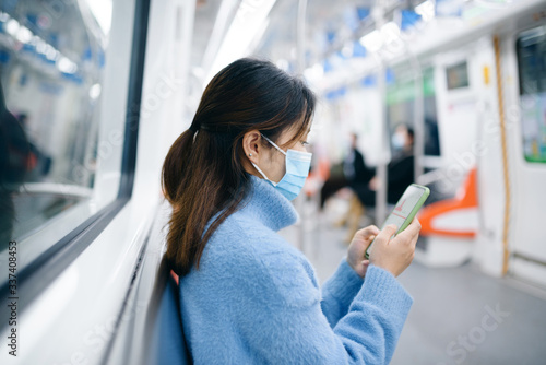 That young Asian woman wearing a surgical mask is using smart phone in the subway.
