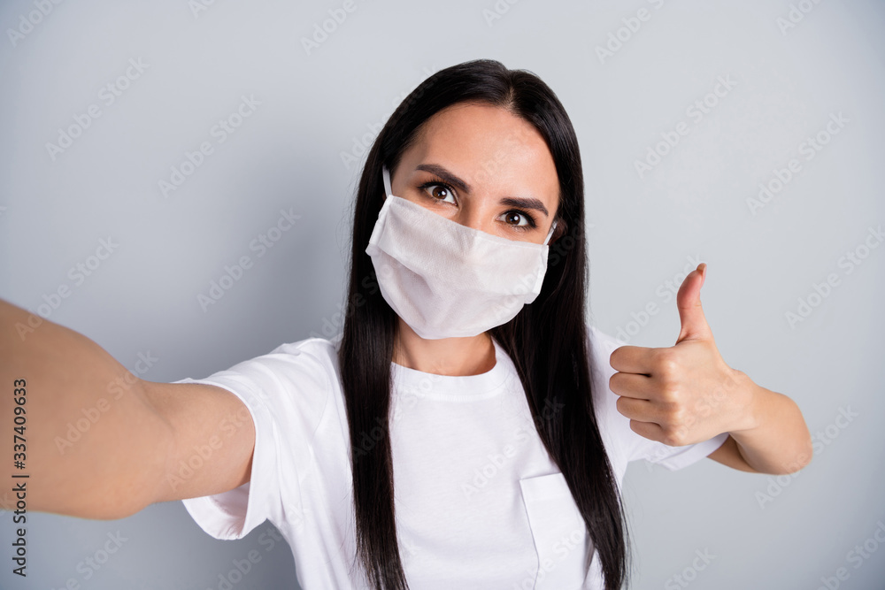 Close up photo positive corona virus quarantine girl make selfie blogging approve self isolation safety quality medical mask show thumb up sign wear t-shirt isolated gray color background Close up photo positive corona virus quarantine girl make selfie blogging approve self isolation safety quality medical mask show thumb up sign wear t-shirt isolated gray color background