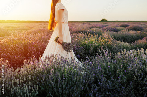 Romantic woman with bouquet of lavender in field having vacation in Provence, France. Girl admires the sunset in lavender fields. Copy space.