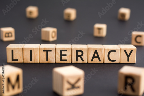 Literacy - word from wooden blocks with letters, literacy the ability to read and write concept, random letters around black background