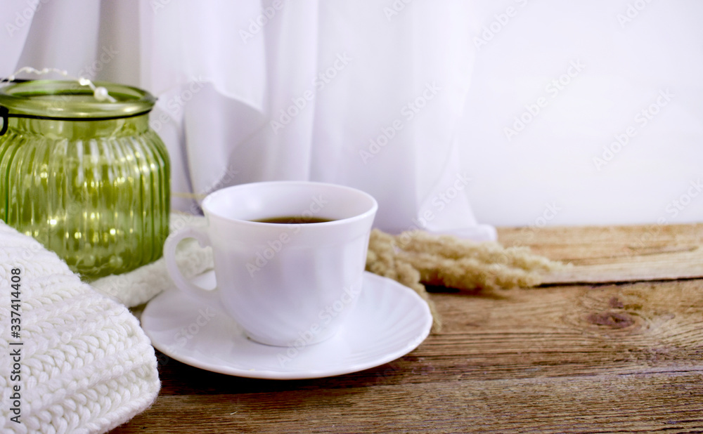 Fototapeta premium Still life hygge kitchen details on desktop. Coffee cup, blanket and light glass on wooden desk. Mock up autumn relax concept.