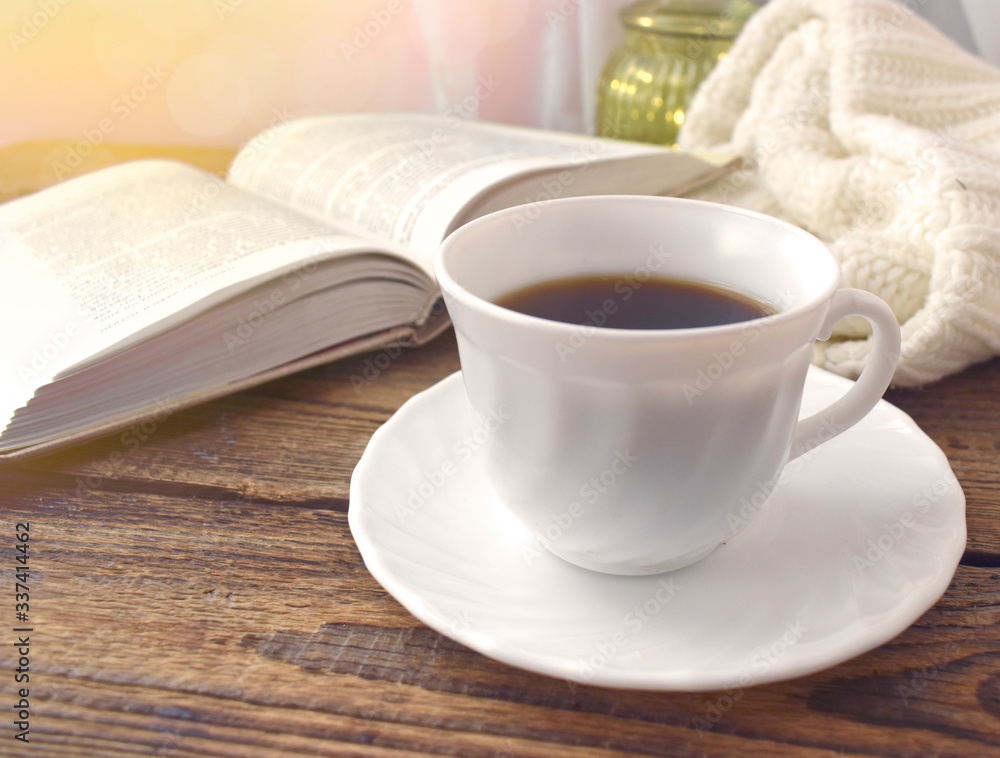 Close up still life detail concept. Coffee cup and book on wooden desk. Cozy home. Hygge style. Sunlight effect.