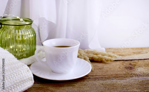 Still life hygge kitchen details on desktop. Coffee cup, blanket and light glass on wooden desk. Mock up autumn relax concept.