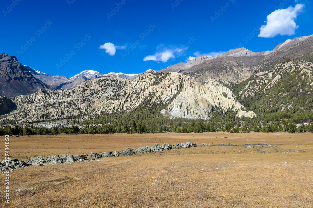 A panoramic view on Annapurna Chain, along Annapurna Circuit Trek in Nepal. There is a vast, dried plain around her and high Himalayan chain in the back. Serenity and calmness.