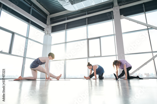 Group of young females keeping one knee on mat while stretching legs forwards
