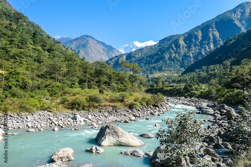 A panoramic view on river and Himalayas from Annapurna Circuit Trek, Nepal. Turquoise color of the river, big stones popping out of the river. Green forest around. Idyllic landscape. photo