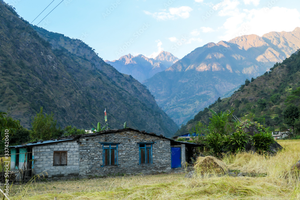 A small cottage along Annapurna Circuit Trek in Himalayas, Nepal. There are high mountain chains around it. Steep and barren slopes. Few prayer flags hanged on the rooftops. Serenity and calmness.