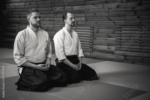 Two men in a kimono sit in seiza and practice meditation in a dojo