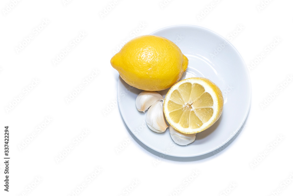 Cloves of garlic. Ripe, juicy, yellow lemon and half a lemon on a white plate. Isolated object on a white background Cloves of garlic. Ripe, juicy, yellow lemon and half a lemon on a white plate. Isolated object on a white background