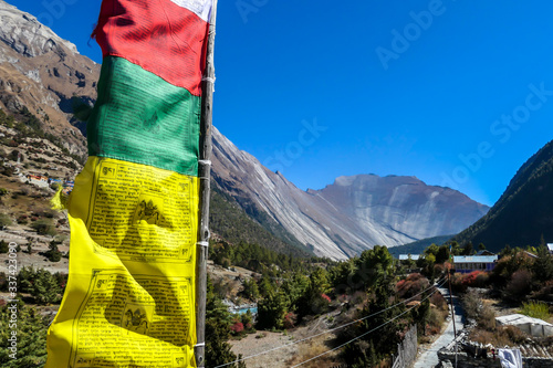 Colorful prayer flags attached to the rooftop waving above the Himalayan peaks along Annapurna Circuit Trek, Nepal. Meditation and peace of mind. High mountains peaks in the back. photo