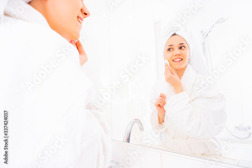 A young woman washing her face with a cotton pad. Facial skin cleansing at home. Makeup Remover. The girl rubs her face with lotion in the bathroom.