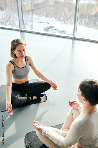 Two young relaxed women in activewear sitting on mats in front of each other