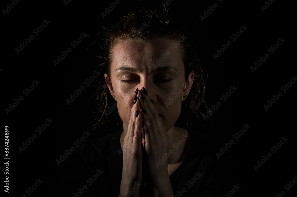 Young woman pray in the dark on a black background Young woman pray in the dark on a black background