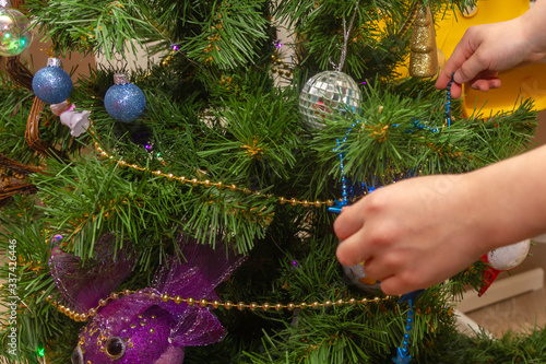 Decorate the Christmas tree at home with balloons and garlands for the New year. A European child hangs glass balls on the Christmas tree.