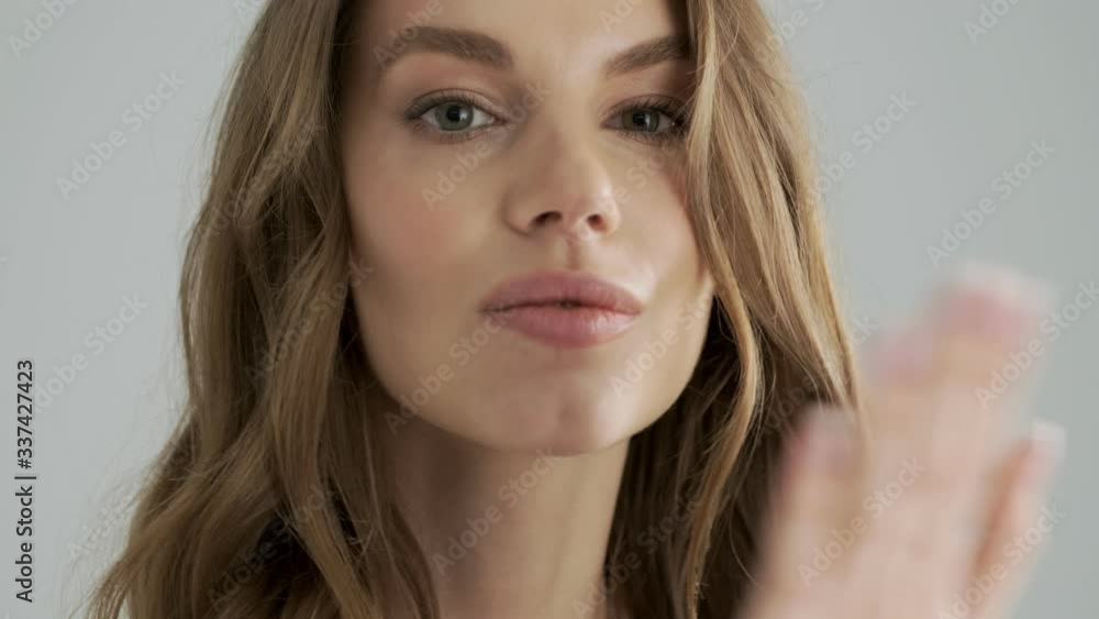 A close-up view of a flirty seductive woman is sending an air kiss to the camera isolated over a gray background in studio A close-up view of a flirty seductive woman is sending an air kiss to the camera isolated over a gray background in studio