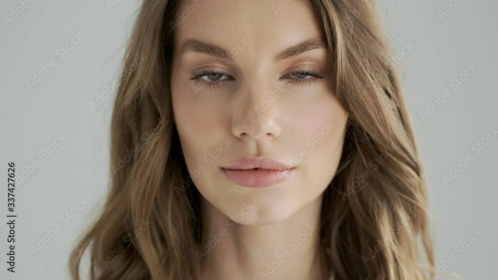 A close-up view of a calm woman is opening her eyes to the camera isolated over a gray background in studio A close-up view of a calm woman is opening her eyes to the camera isolated over a gray background in studio