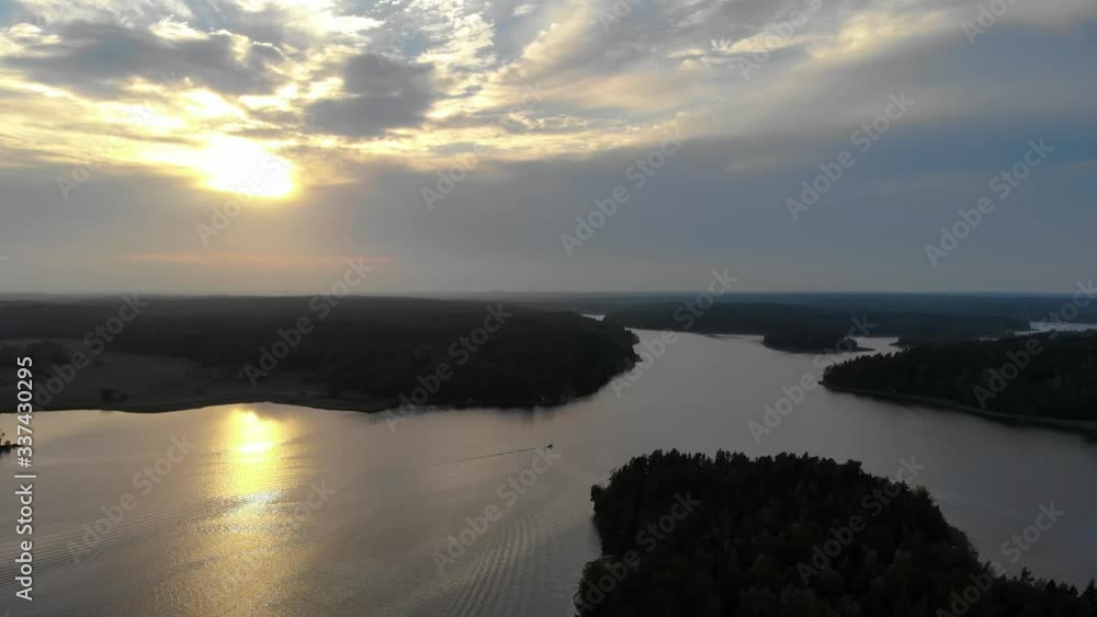 Aerial shot flying over archipelago water with a colorful sunset in background Aerial shot flying over archipelago water with a colorful sunset in background