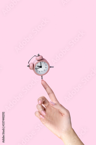 Fototapeta Naklejka Na Ścianę i Meble -  Alarm clock balancing on womans hand on pink background