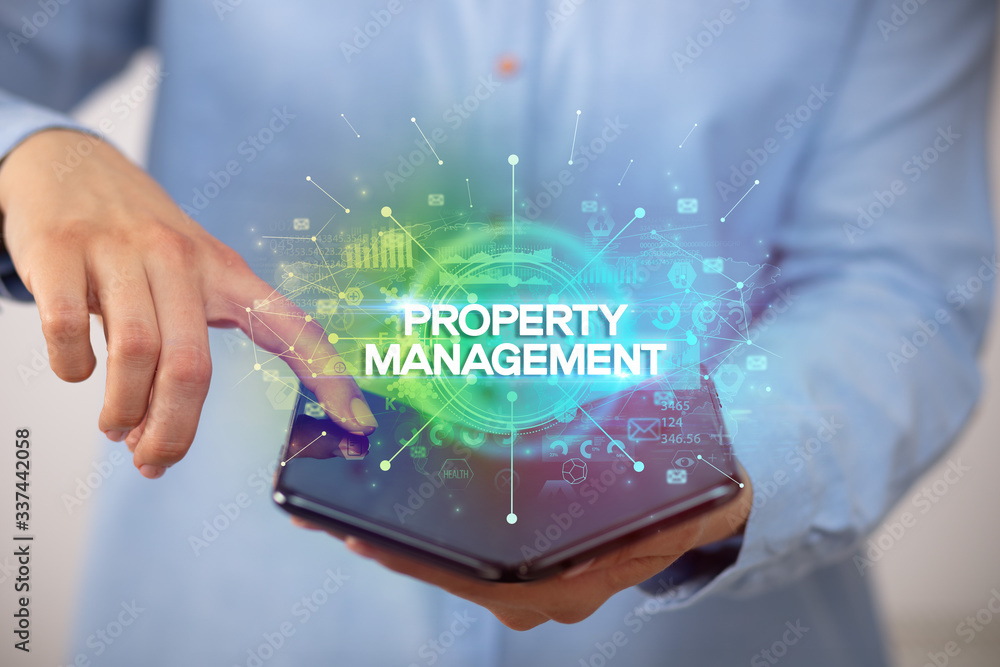 Businessman holding a foldable smartphone with PROPERTY MANAGEMENT inscription, new business concept Businessman holding a foldable smartphone with PROPERTY MANAGEMENT inscription, new business concept