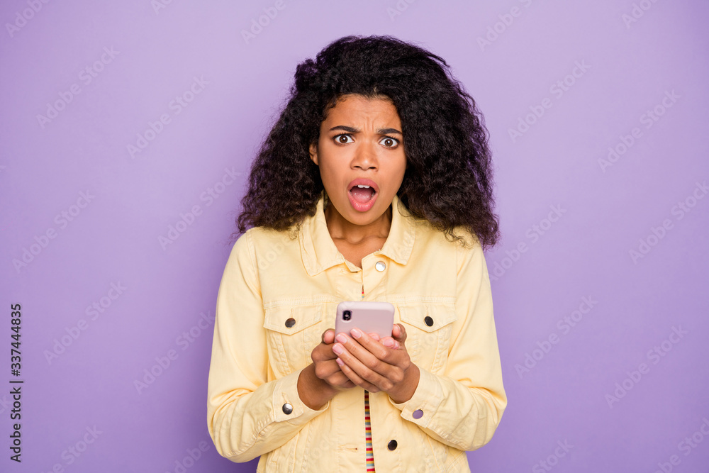Photo of casual afraid scared frightened woman expressing negative emotions on face knowing bad news in yellow shirt isolated with phone on pastel violet color background