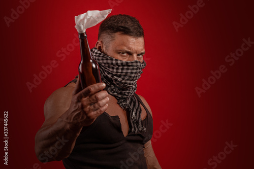 Young male athlete protester with a closed face with a Molotov cocktail in hands posing on a red background