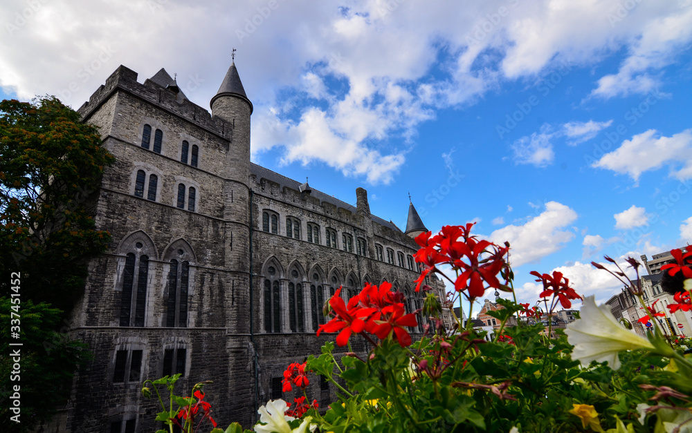 Ghent,Belgium,August 2019.Geraard de Duivelstraat Castle.The main facade overlooks the water: it is an example of the medieval buildings of the city.Blue sky with white clouds.Planters along the canal