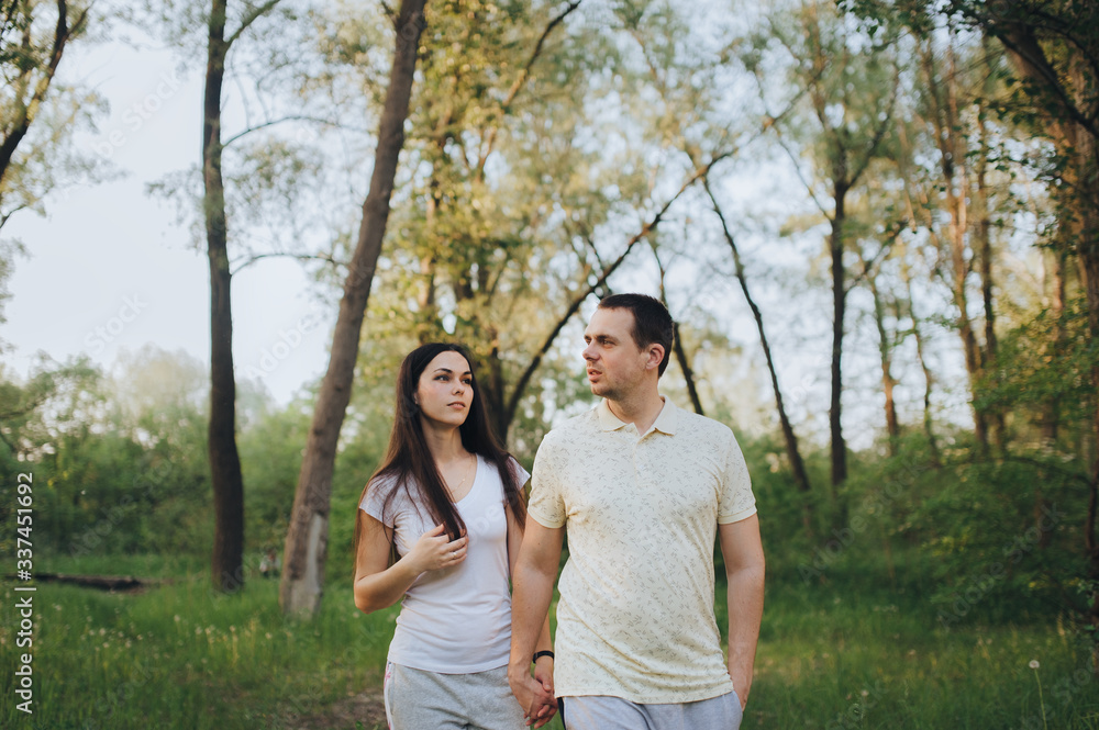 Fototapeta premium Loving, beautiful, stylish guy and girl in tracksuits strolling through the forest, holding hands, outdoors in the park. Love story newlyweds. Photography, concept.