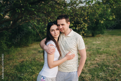 Lovers, beautiful, stylish guy and a girl in tracksuits hug in the forest, outdoors in a green garden. Love story newlyweds. Photography, concept.