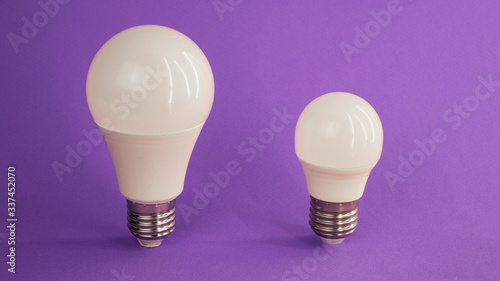 two light bulbs of different sizes stand on a purple background photo