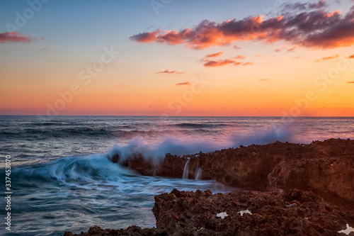 Splash of seawater at colorful sunset on coral rocks. Caribbean Cuba