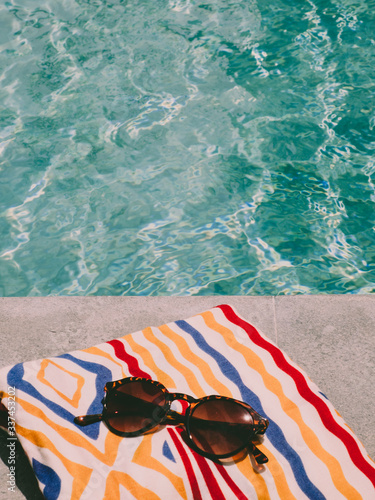 Cuadro en lienzo A colourful bath towel and a pair of sunglasses at a swimming pool