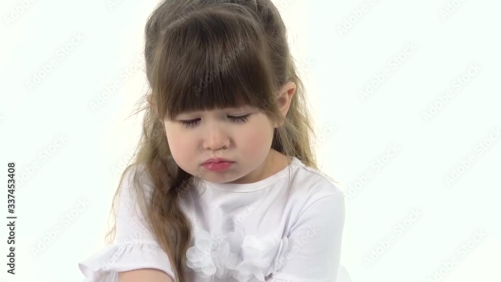 Cute little girl puffed out her cheeks and sitting offended on white background. Child emotion. Slow motion. Close up Cute little girl puffed out her cheeks and sitting offended on white background. Child emotion. Slow motion. Close up