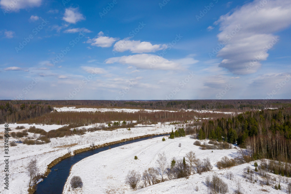 View of the Uvod River with snowy banks and a blue sky with white clouds.