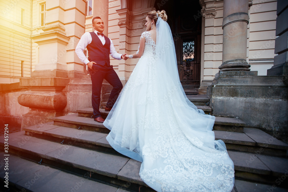 Obraz premium The bride and groom walk together in the park. Charming bride in a white dress, the groom is dressed in a dark elegant suit.
