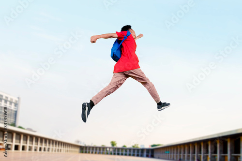 University student jumping in the air with his bag