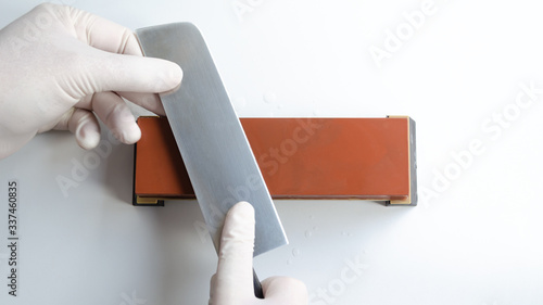 Man with white gloves sharpening a japanese Nakiri knife with whetstone sharpener or grindstone on white background photo