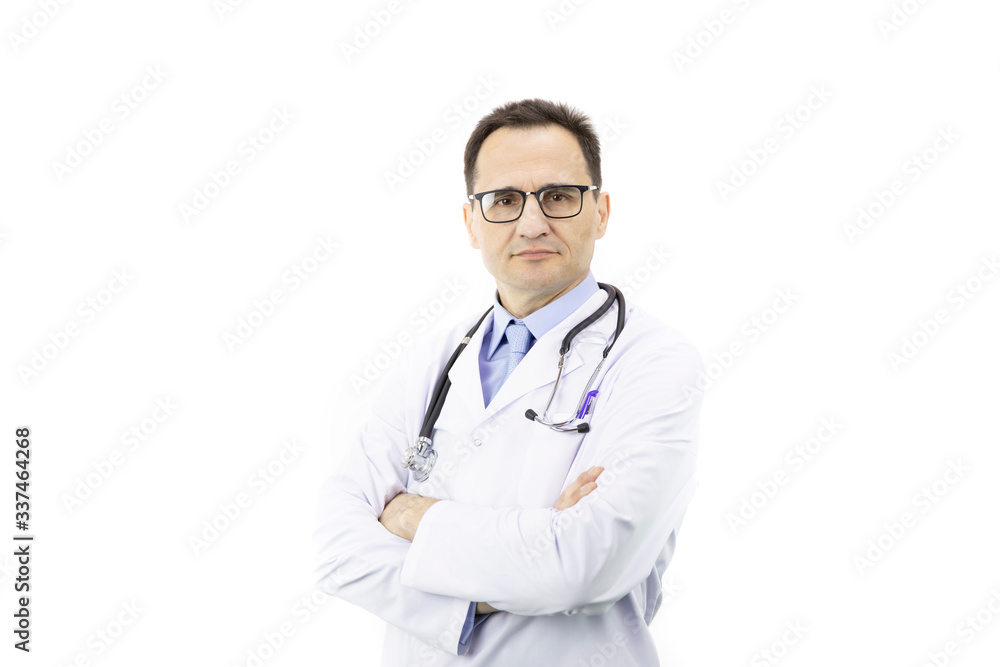 The surgeon with glasses in a white coat with a stethoscope stands on a white background and looks at the camera. Hands are folded on the chest. Serious stern look. Portrait of a doctor. Close-up The surgeon with glasses in a white coat with a stethoscope stands on a white background and looks at the camera. Hands are folded on the chest. Serious stern look. Portrait of a doctor. Close-up