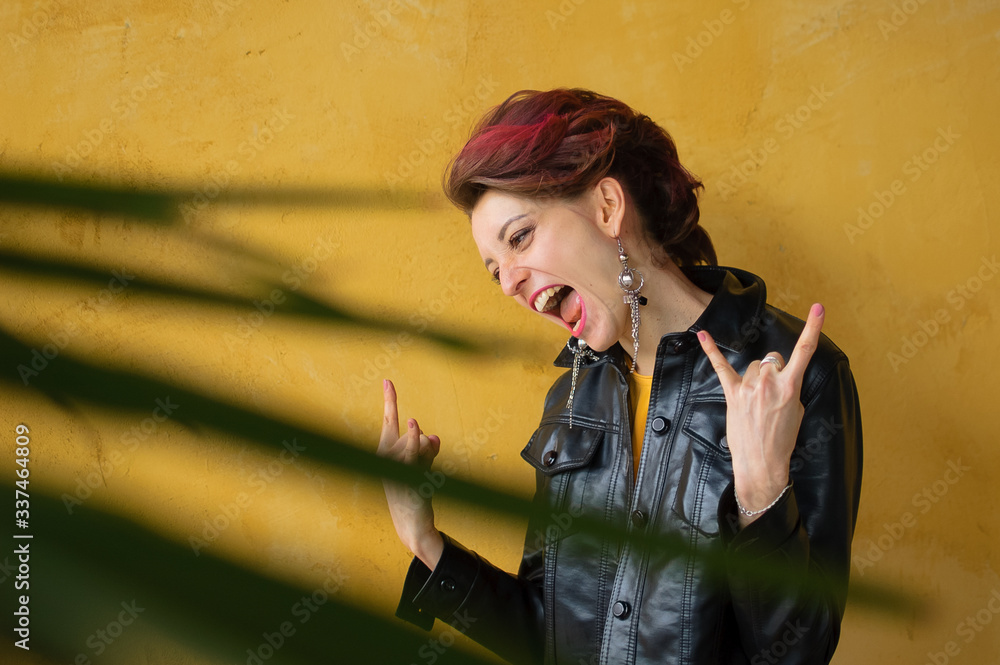 Obraz premium Let's rock concept. Portrait of excited beautiful woman with dark pink hair in casual yellow dress standing, looking at camera, showing rock and roll gesture.