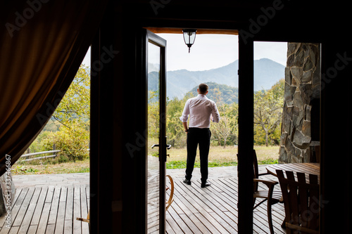 Happy man standing in terrace at home drinking coffe with view of rocky mountains during autumn © nazariykarkhut