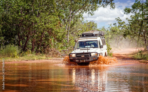 Western Australia – Flooded Outback gravel road with 4WD car crossing the waterhole with splashing muddy water at the savanna photo