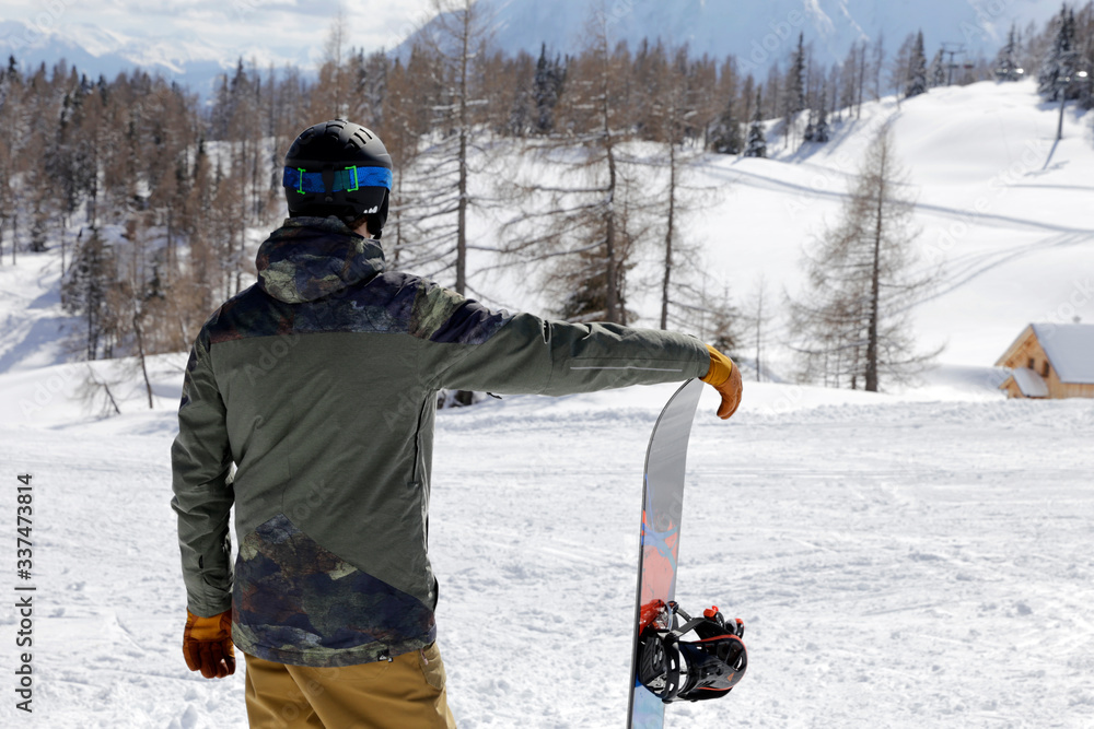Young man standing and enjoying the view. Man standing with snowboard on winter holiday. Winter sport, active lifestyle. 