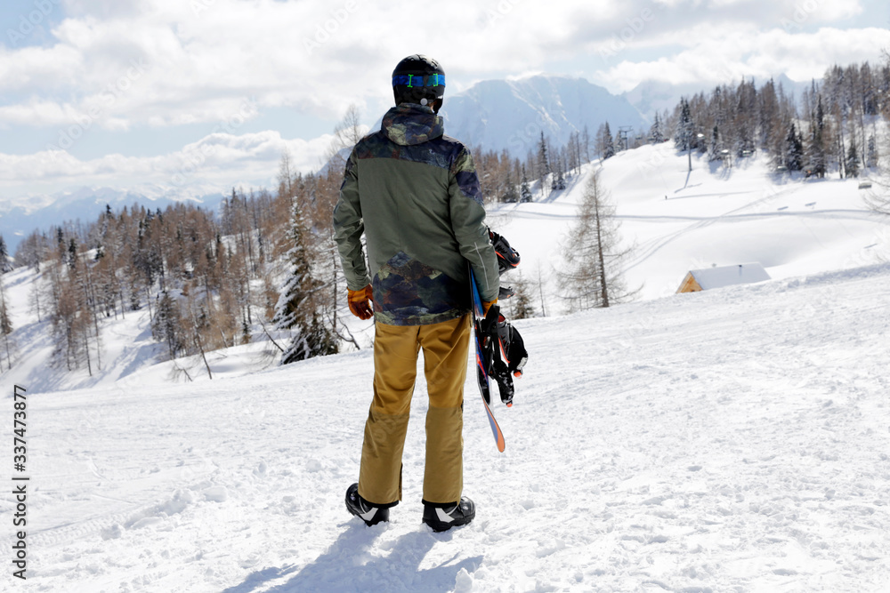 Young man standing and enjoying the view. Man standing with snowboard on winter holiday. Winter sport, active lifestyle. 