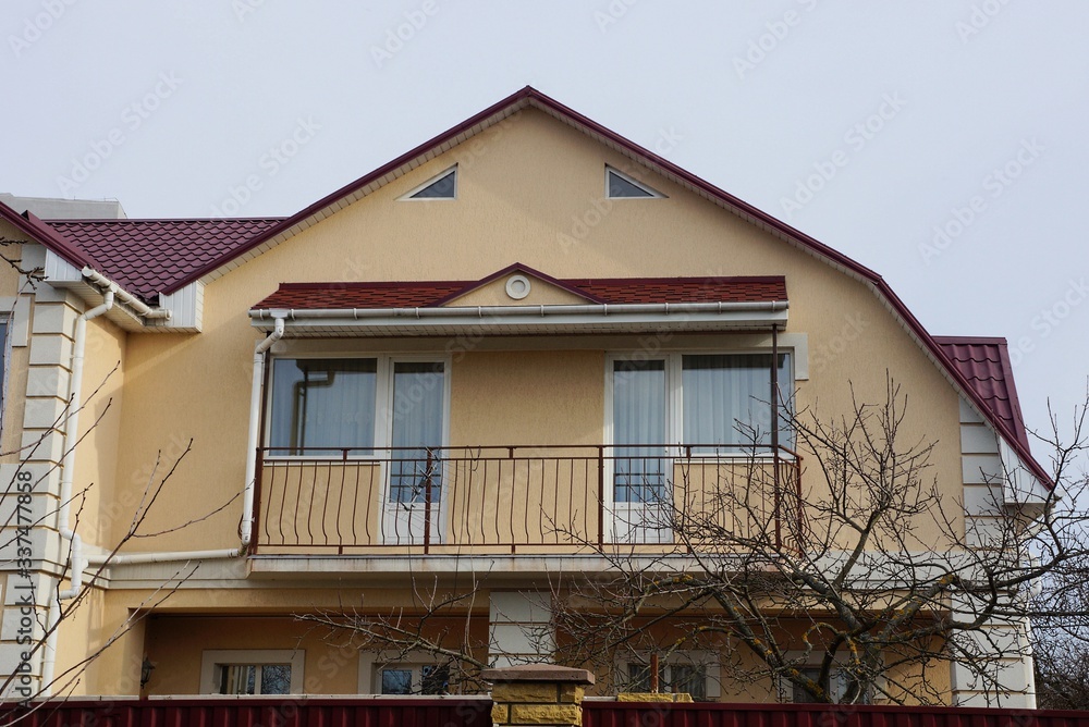 facade of a brown private house with an open black iron balcony against a gray sky