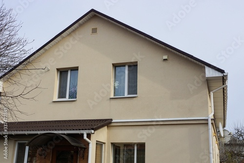 part of a large private house with a brown wall and white windows under a tiled roof  © butus