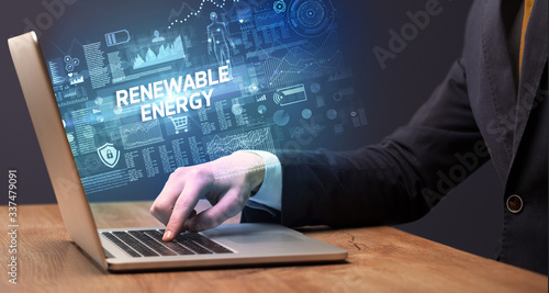 Businessman working on laptop with RENEWABLE ENERGY inscription, cyber technology concept