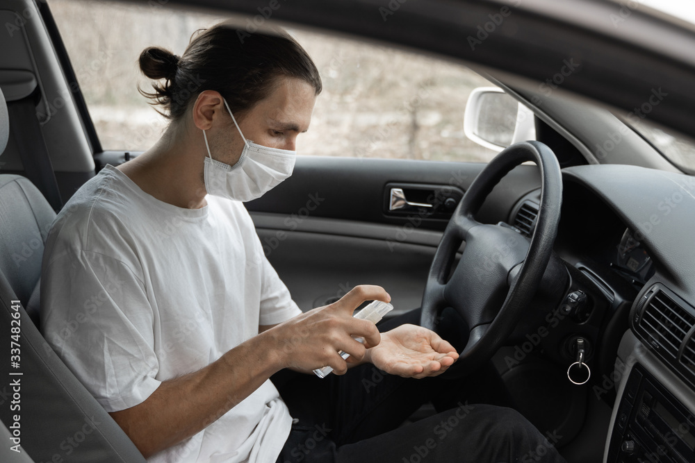Man in protective medical mask is using antiseptic for protect himself from bacteria virus while planning to drive. Protective mask while quarantine, pandemic, covid 19, coronavirus, infection.