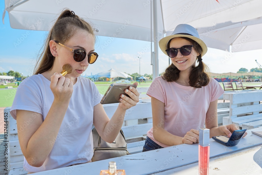 Two teenage girls making make-up, sitting in summer outdoor cafe Two teenage girls making make-up, sitting in summer outdoor cafe